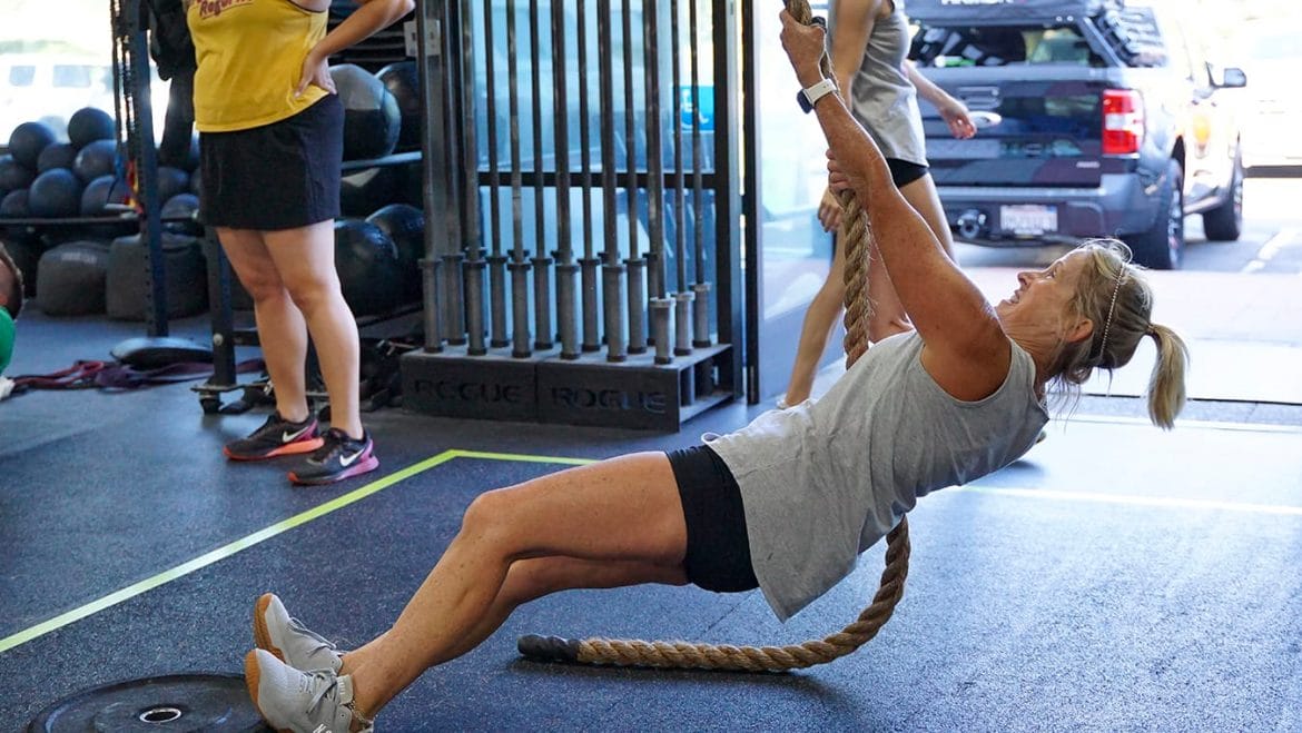active woman in gym pulling herself up with a rope